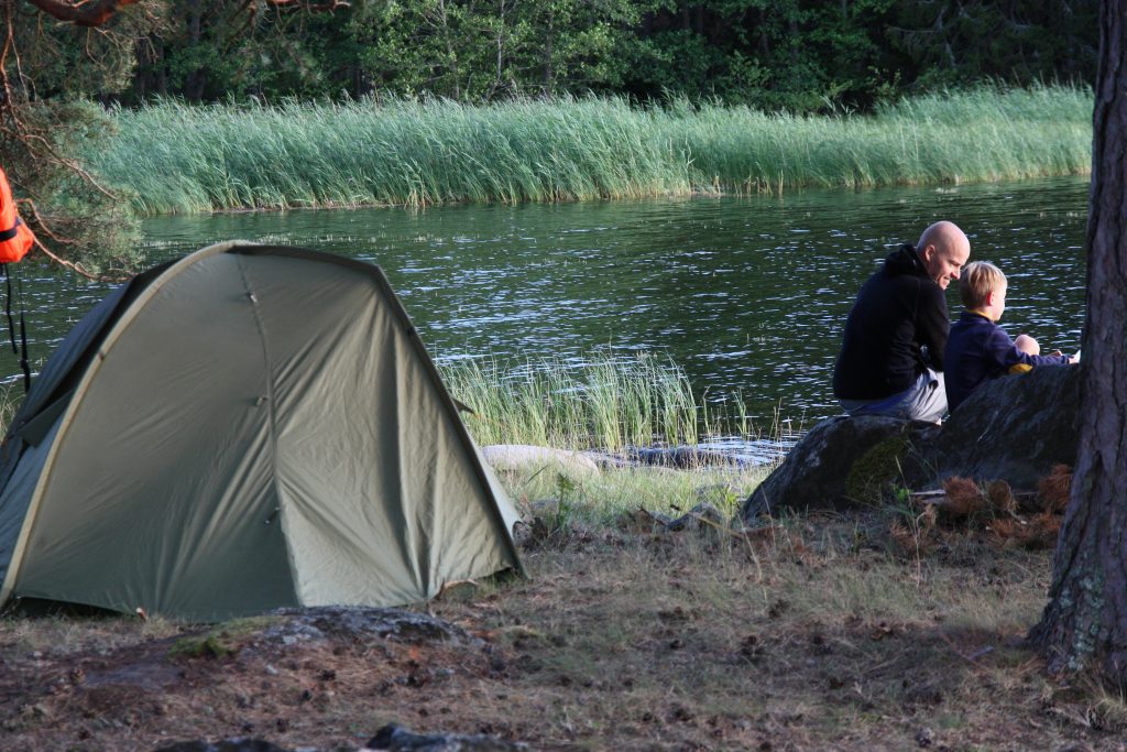 A man and a boy sitting by their tent and the water.