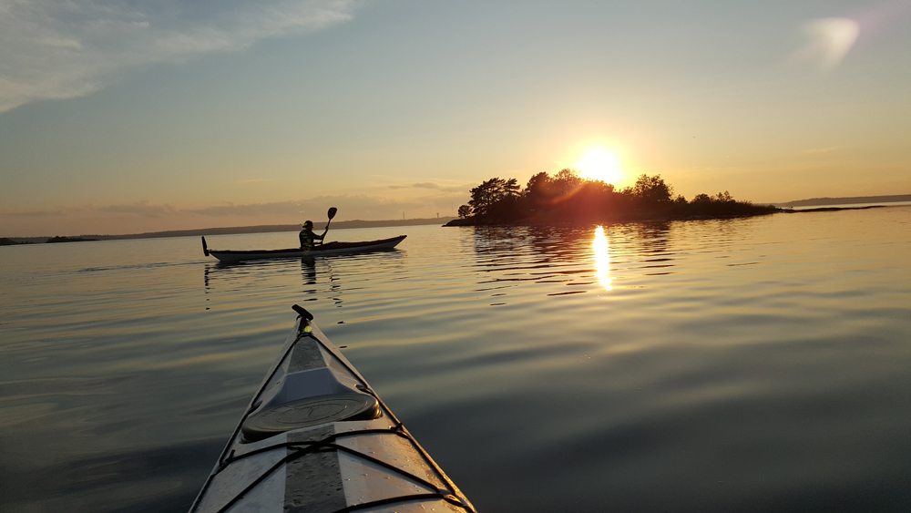 En kanot på vindstilla vatten i solnedgången utmed den västra sidan av Sävö